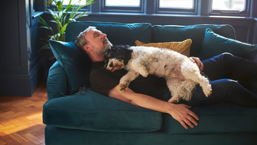Man asleep on a green couch with a dog sleeping on his chest.