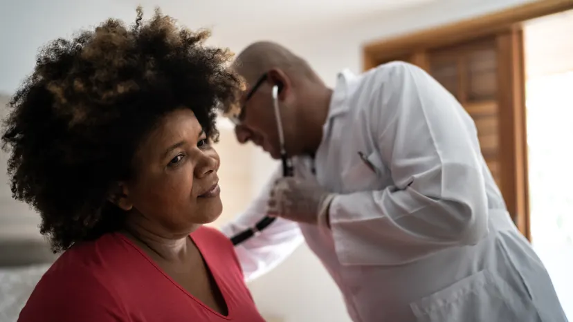 Middle aged woman getting her heart checked out by a doctor listening through a stethoscope.
