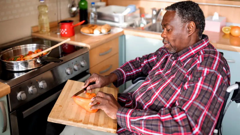 Man with multiple sclerosis chopping vegetables and cooking them in a pan on the stove.