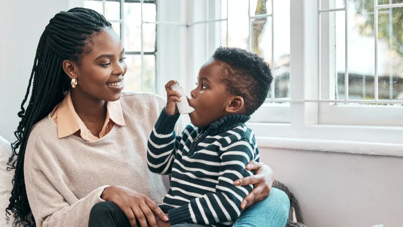 Young boy with asthma using his inhaler while sitting in his mother's lap