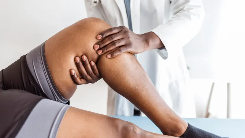 African American doctor examining a female patient's knee to diagnose rheumatoid arthritis