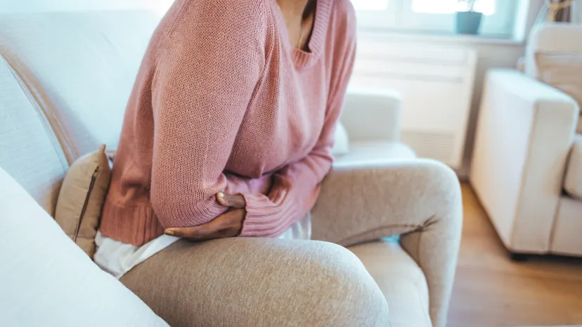 Cropped shot of a young woman sitting on her couch holding her painful abdomen suffering from Crohn's disease symptoms