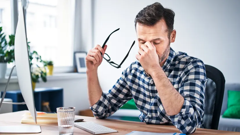 View of man at his desk, eyes closed, holding his glasses with one hand and his head with the other, fatigued from anemia