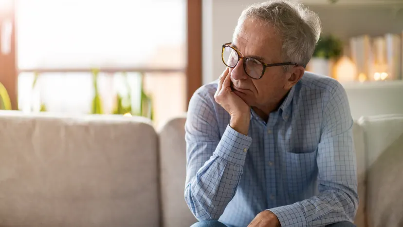 Mature man sits in his living room, head in hand looking worried about his Parkinson's diagnosis