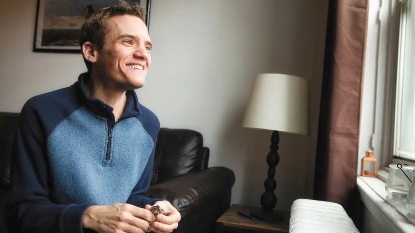 Man with autism looks out of a bright window while he plays with a fidget ring