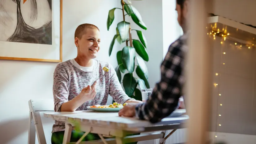 Woman with leukemia sits at a dining table eating