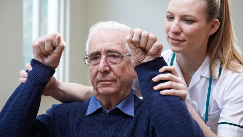 Young female nurse assessing a senior man stroke victim by raising his arms