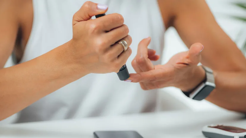Prediabetic woman doing a finger prick to measure haemoglobin A1C blood glucose levels, using smart phone app