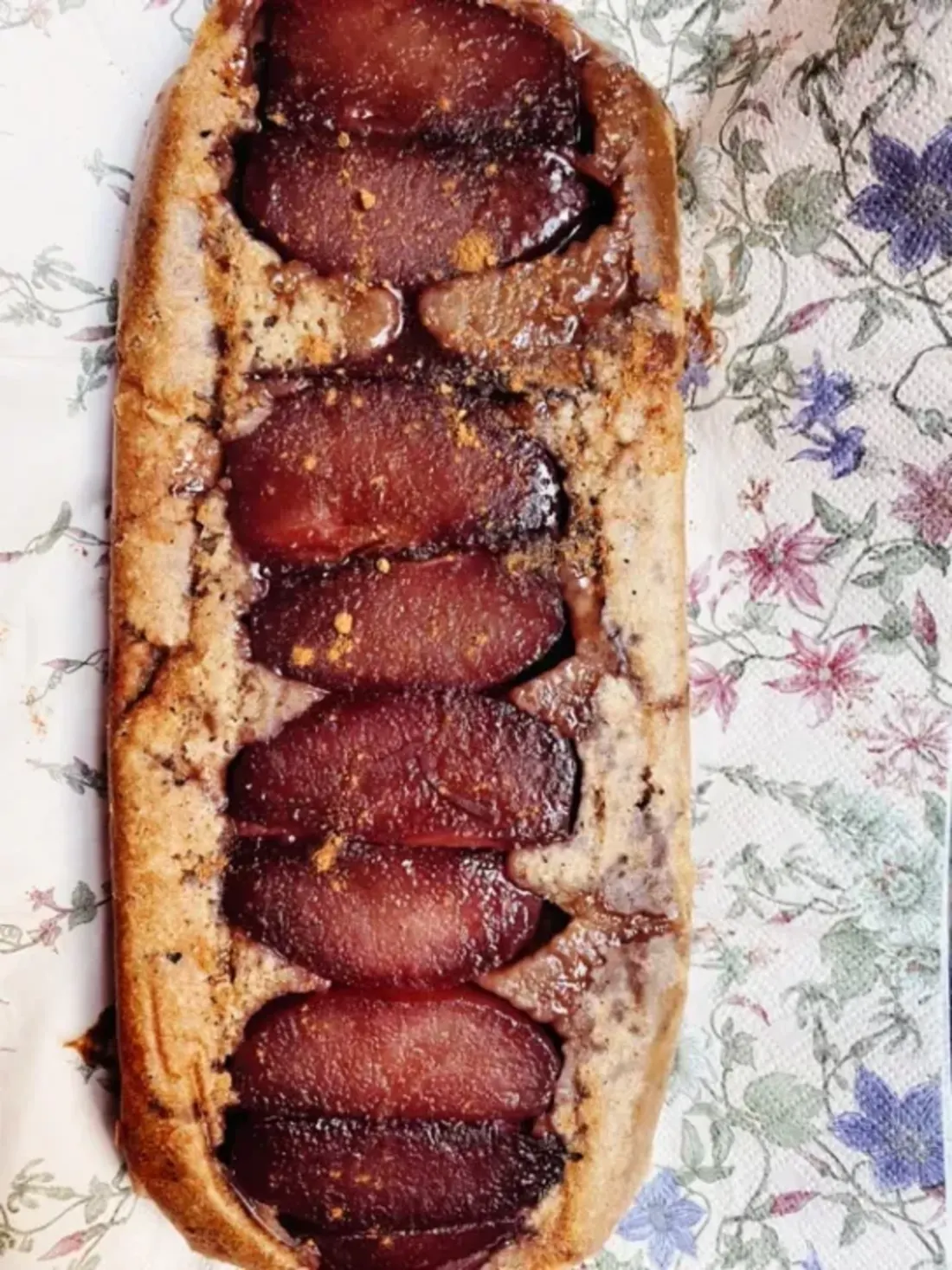 Een servet met bloemen. Hier bovenop ligt een langwerpige stoofperencake. De kleuren van de stoofperen zijn paars-aubergine achtig. 