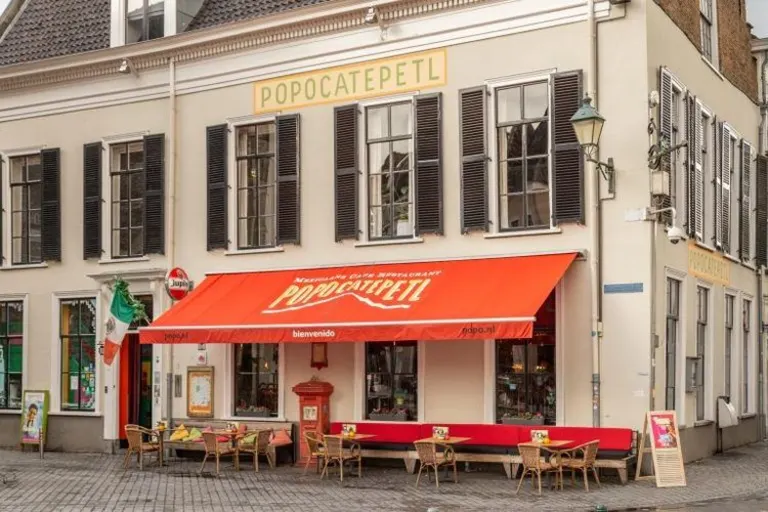 Een wit pand met daarop Popocatepetl.Je ziet een oranje luifel met de naam van het restaurant erop