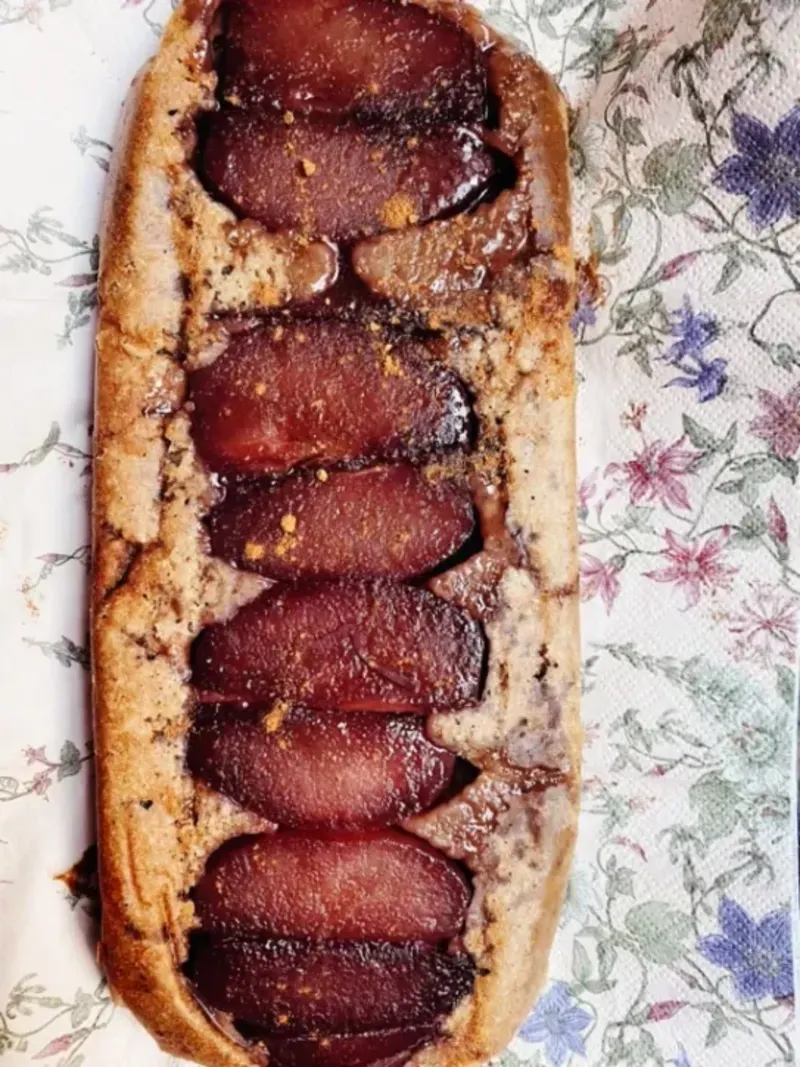 Een servet met bloemen. Hier bovenop ligt een langwerpige stoofperencake. De kleuren van de stoofperen zijn paars-aubergine achtig. 