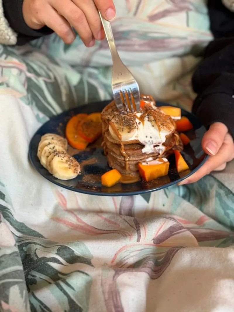 Een persoon onder de deken die een bord met pancakes vast houdt
