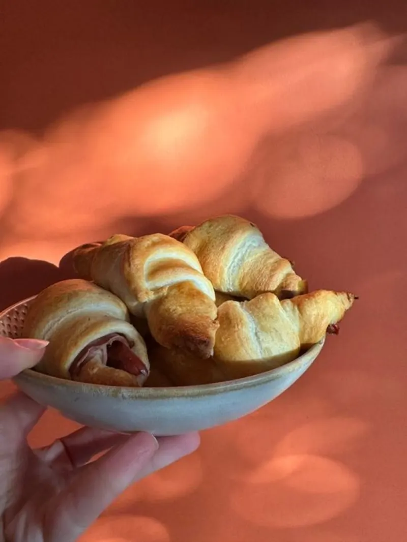 Een schaaltje gevuld met ham-kaas croissants voor een rode achtergrond