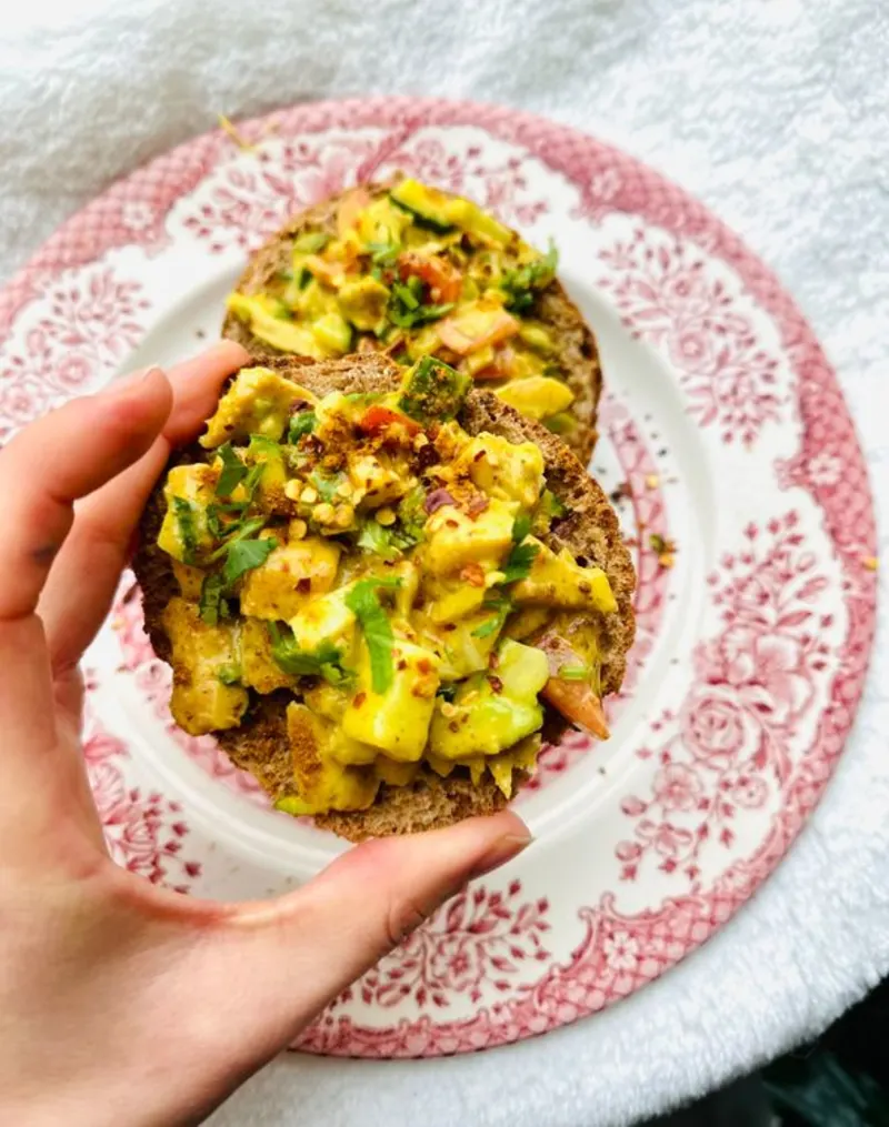 Een hand die een broodje met vegan kip kerrie salade vast houdt
