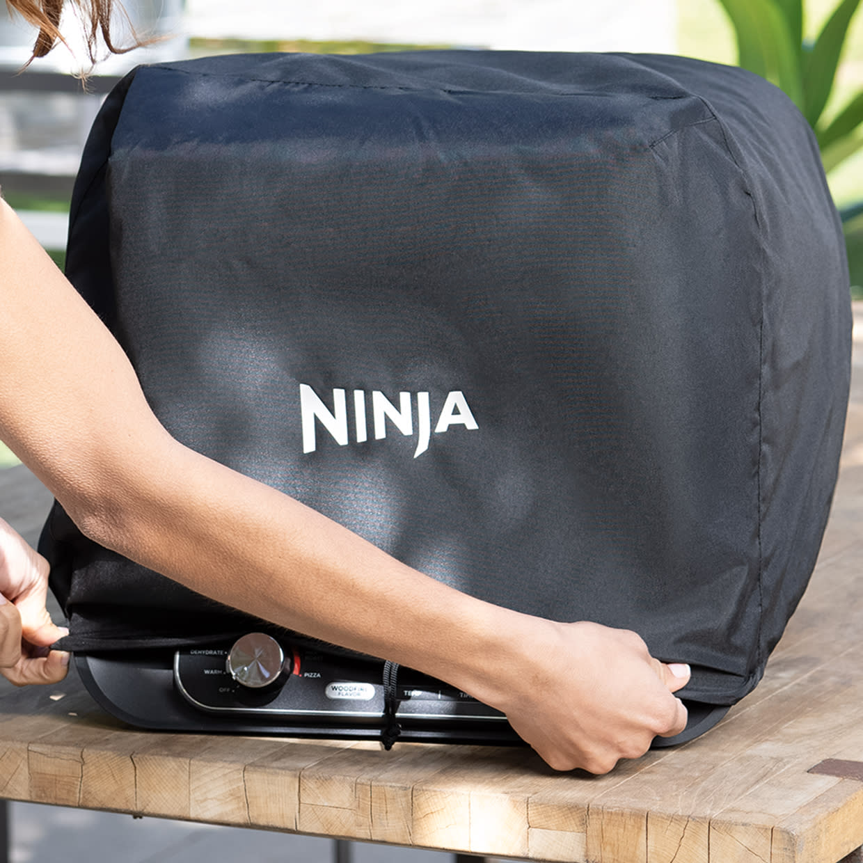 https://res.cloudinary.com/sharkninja-na/image/upload/v1686242670/NinjaUS/Category/Outdoor%20oven/6%20Build%20the%20Ultimate%20set%20up/2%20Premium%20Oven%20Cover/R_OO101_InUse_Tightening_Cover_Woman1.jpg