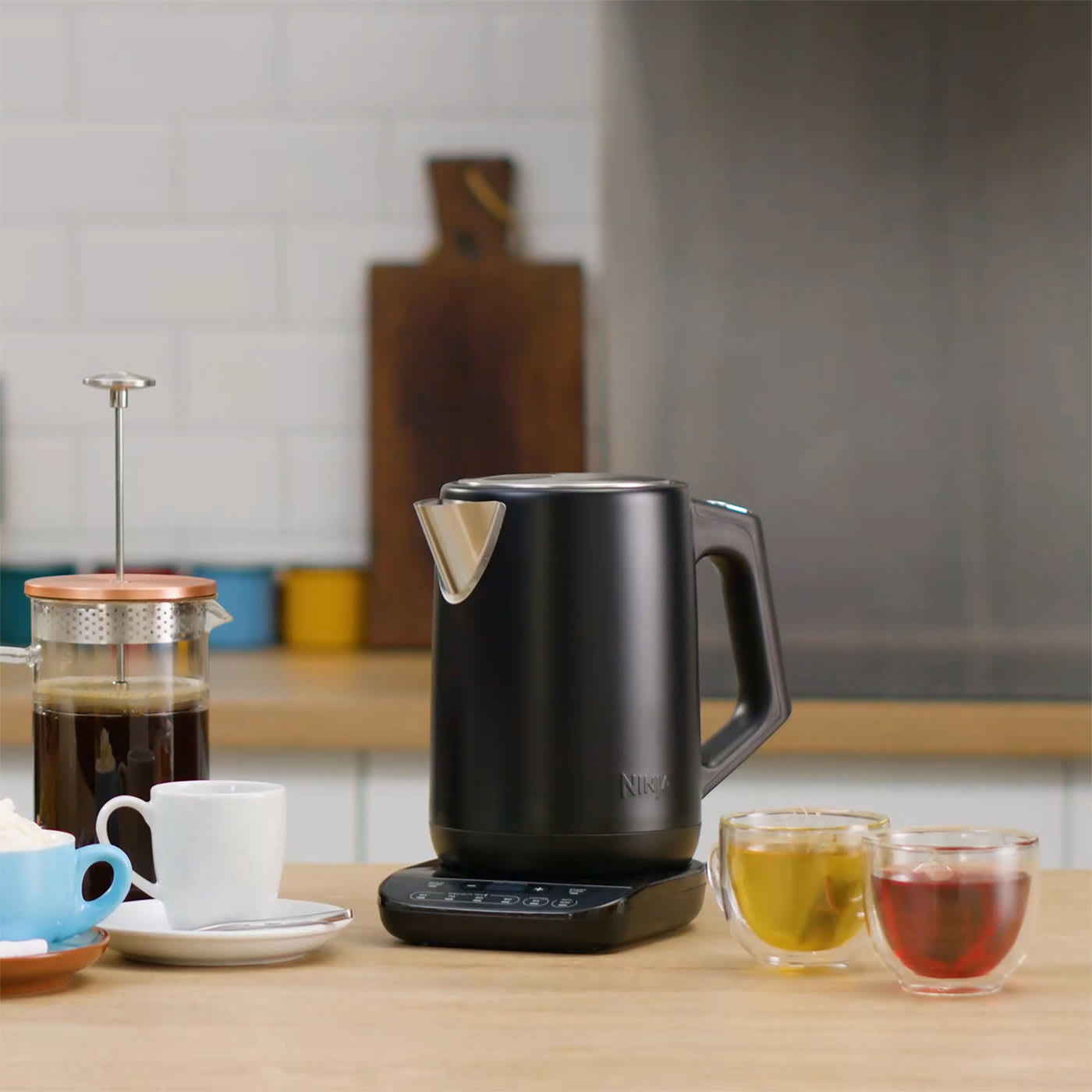 Imagen de un hervidor de agua Ninja color plateado con tazas de té alrededor