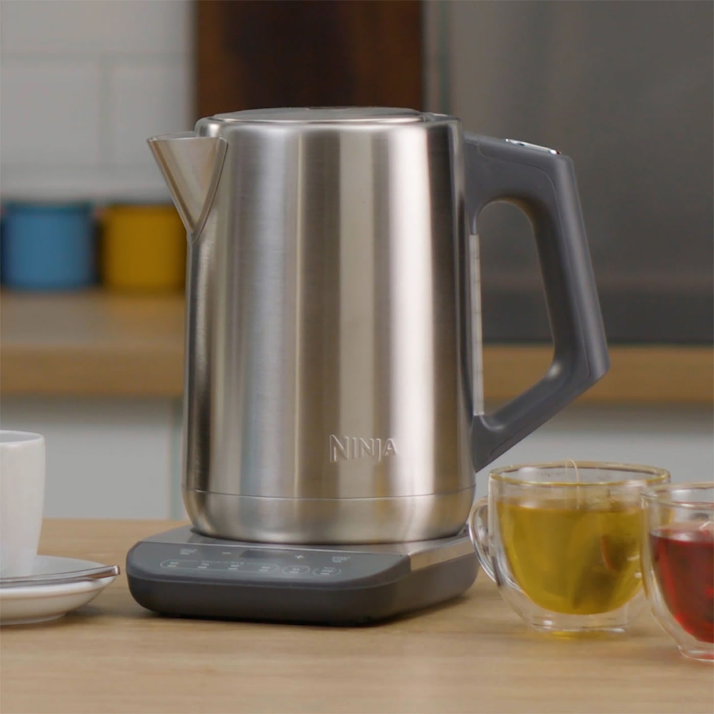 Imagen de un hervidor de agua Ninja color plateado con tazas de té alrededor