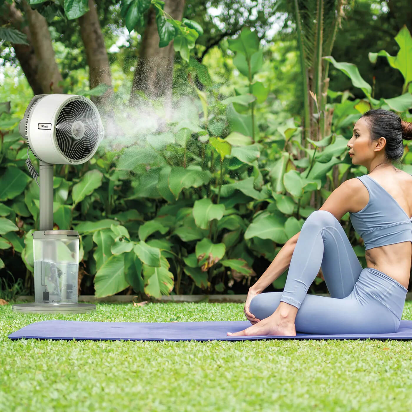 Imagen de mujer sentada al aire libre sobre una esterilla de yoga junto al ventilador Shark FlexBreeze