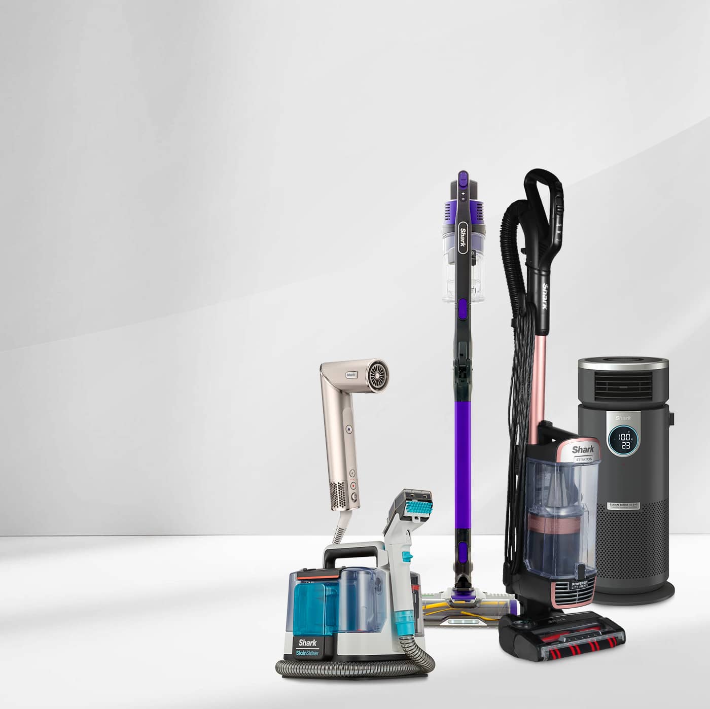 A selection of Shark home appliances, including vacuum cleaners, a steam mop, a hair dryer, and an air purifier, displayed on a light grey gradient background