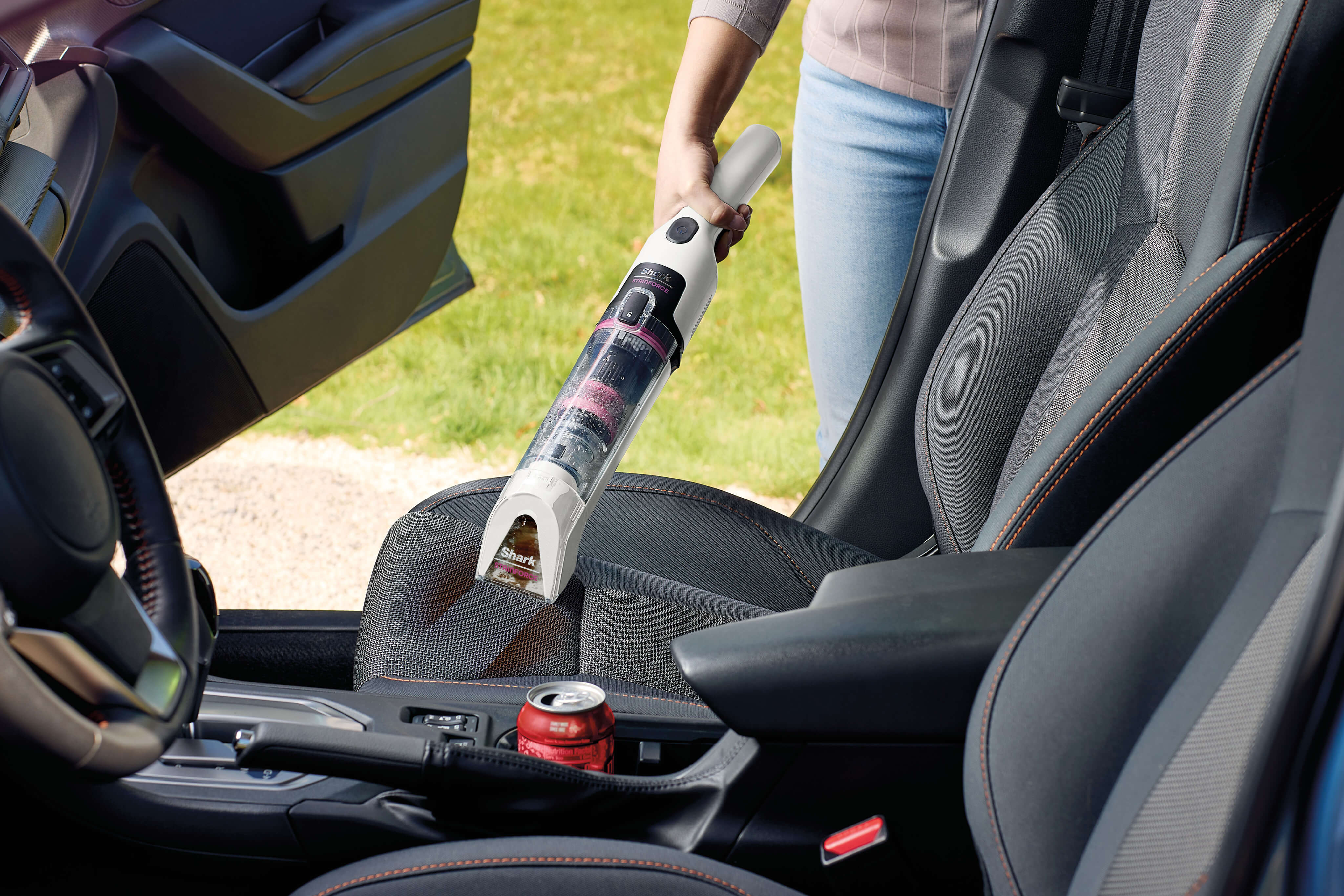 Une personne utilise un aspirateur à main Shark StainForce pour nettoyer l'huile moteur renversée