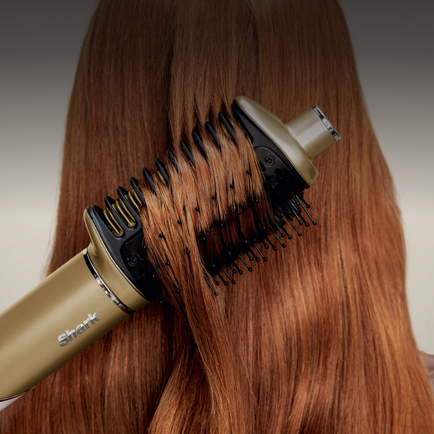 Blonde woman styles her hair with a heated round brush, achieving soft, shiny waves with a glossy finish.