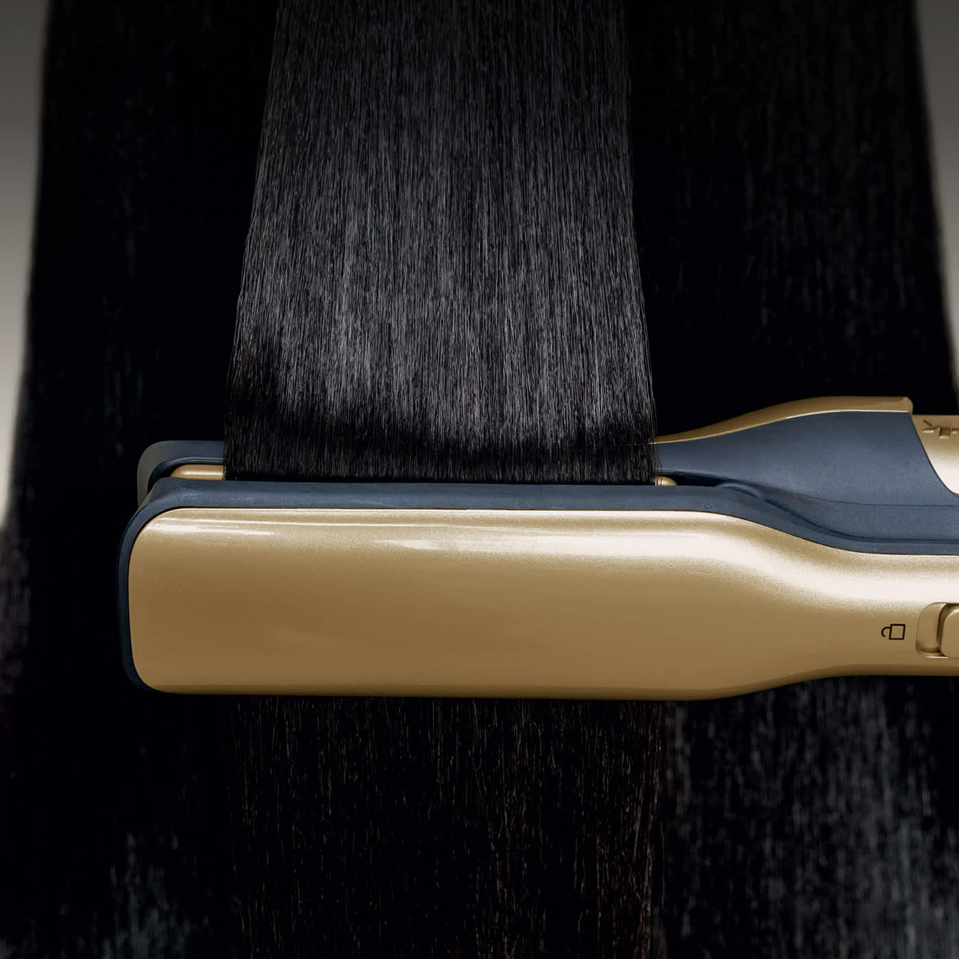 Smiling woman straightens curly hair with a gold flat iron, leaving it smooth and glossy.