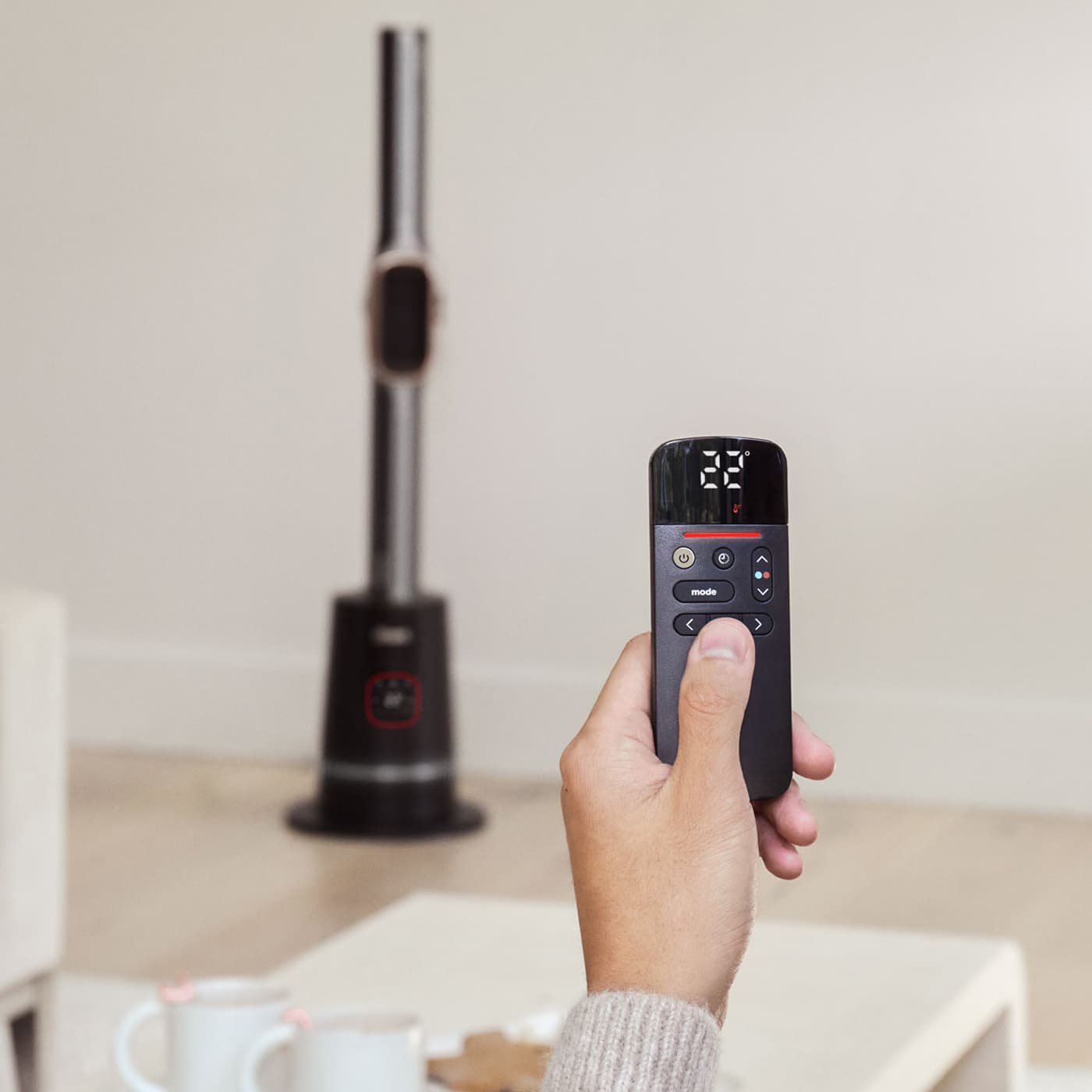 Gros plan d'une main tenant une télécommande avec des boutons d'alimentation, de mode et de direction, pointée vers le Shark TurboBlade