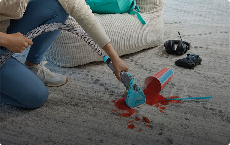 A person using the Shark StainStriker to clean up a drink spill on a carpet