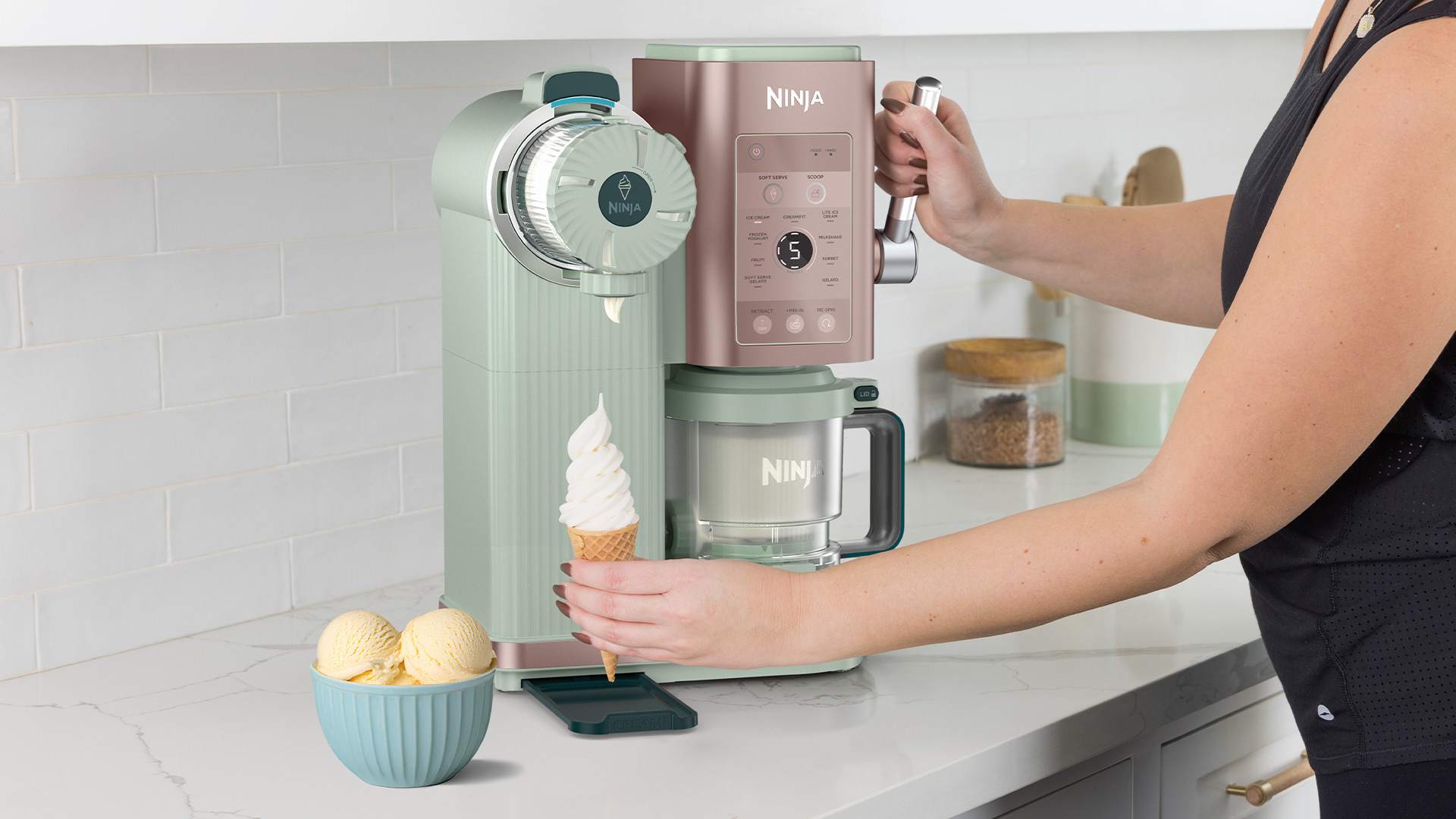 A Ninja Creami machine making mango ice cream on a kitchen counter, with fresh mangoes and a bowl of scoops nearby.