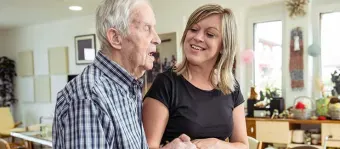 A Visiting Angels caregiver offering comfort and support to an elderly patient receiving palliative care, emphasizing compassion in a serene home setting.