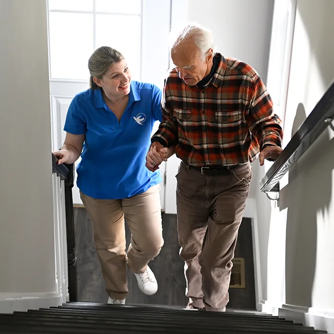 A Visiting Angels caregiver demonstrating proper techniques for using mobility aids with an elderly man, emphasizing fall prevention in a home setting.