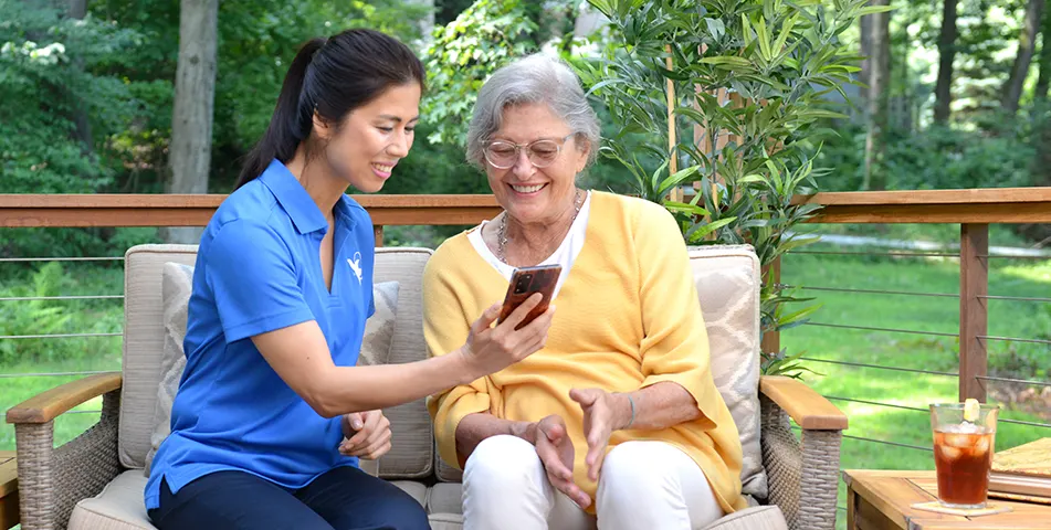 A female Senior Home Care by Angels senior home care provider shows an elderly woman a phone in the yard.