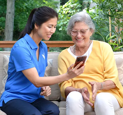A female Senior Home Care by Angels senior home care provider shows an elderly woman a phone in the yard.