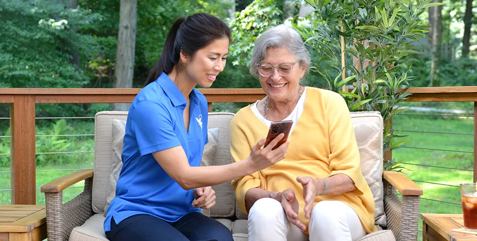 A female Senior Home Care by Angels senior home care provider shows an elderly woman a phone in the yard.