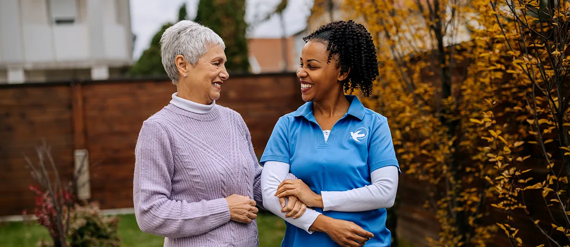 Senior Home Care by Angels female caregiver walks with a senior woman outdoors, providing compassionate senior home care, companionship, and support for independent living.