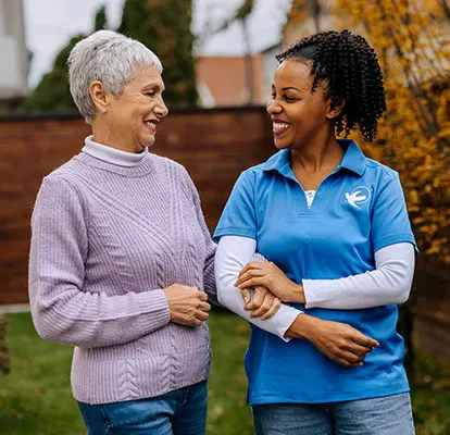 Senior Home Care by Angels female caregiver walks with a senior woman outdoors, providing compassionate senior home care, companionship, and support for independent living.