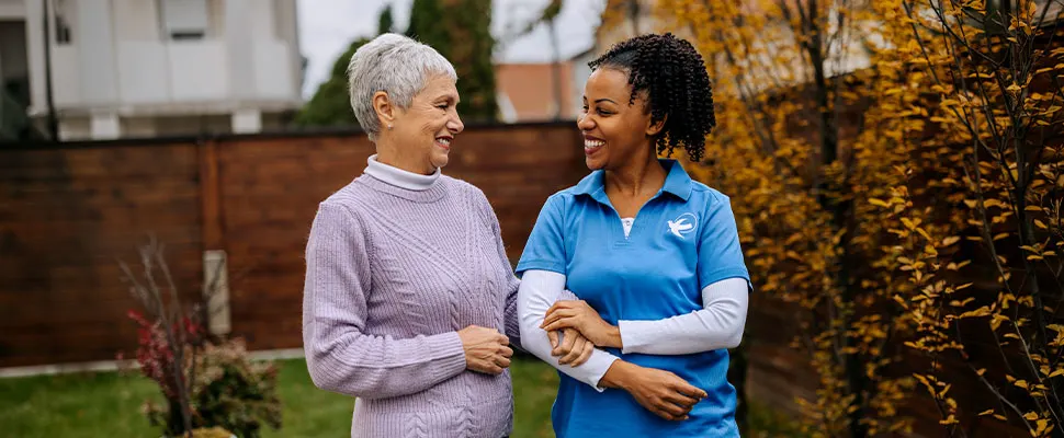 Senior Home Care by Angels female caregiver walks with a senior woman outdoors, providing compassionate senior home care, companionship, and support for independent living.