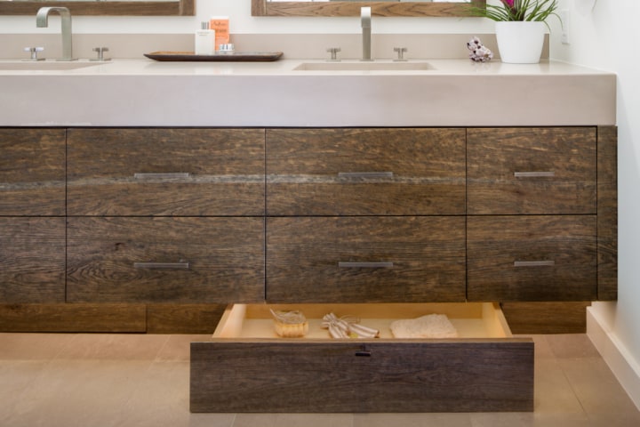 A gorgeous natural wood vanity with white sink. A natural wood toe kick drawer contains various luxurious toiletries.