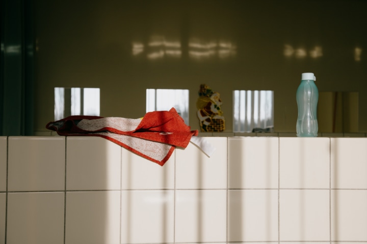 sunlit white square bathroom tiles with orange towel and plastic bottle