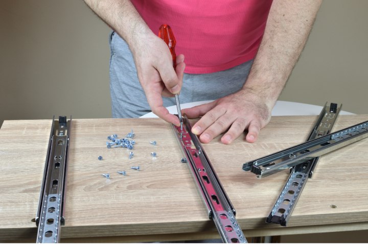 Closeup of man’s hands installing drawer slides on a wooden cabinet