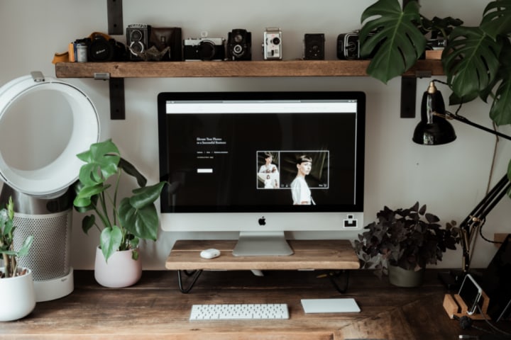 Wooden desk with a Mac, plants, and cameras