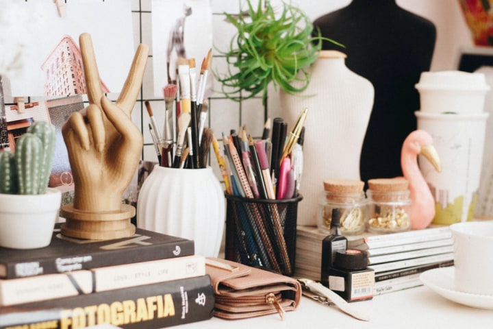  A desk with many stacked books, pots filled with art and writing supplies, and ornaments