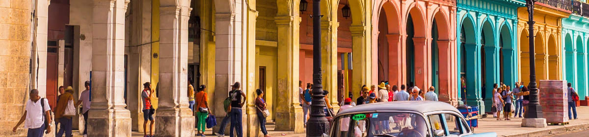 A blue oldtimer taxi is driving through Habana Vieja in front of a colorful facade.