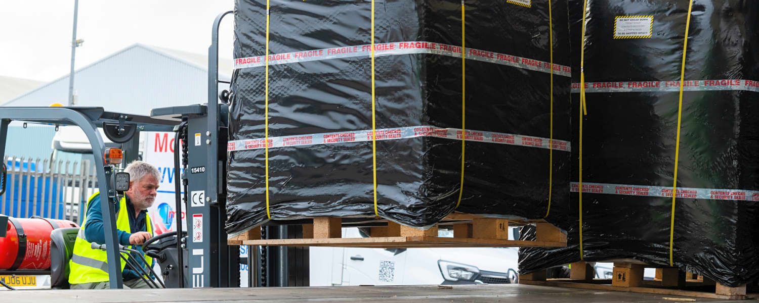 A man in a forklift loading a 1st Move International pallet on to a container transport vehicle for shipping overseas