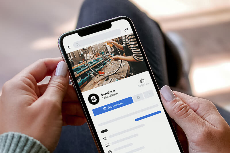 Ein Smartphone, auf dem der "Jetzt buchen" Button auf der Facebook Unternehmensseite zu sehen ist