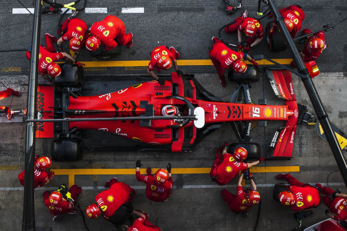 Red Formula 1 race car in the pit with mechanics all around racing to change tires, etc. View from above.