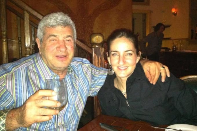 Older man and daughter hugging and holding up a wine glass to the camera