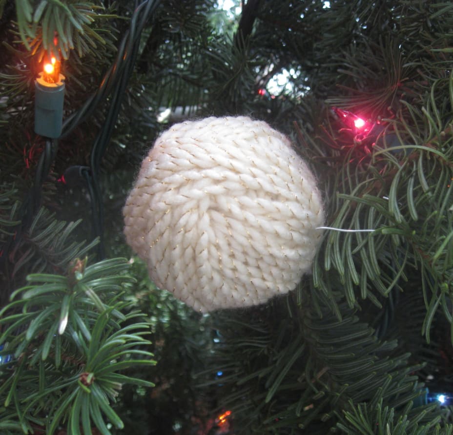 White yarn ball ornament hanging on Christmas tree with lights