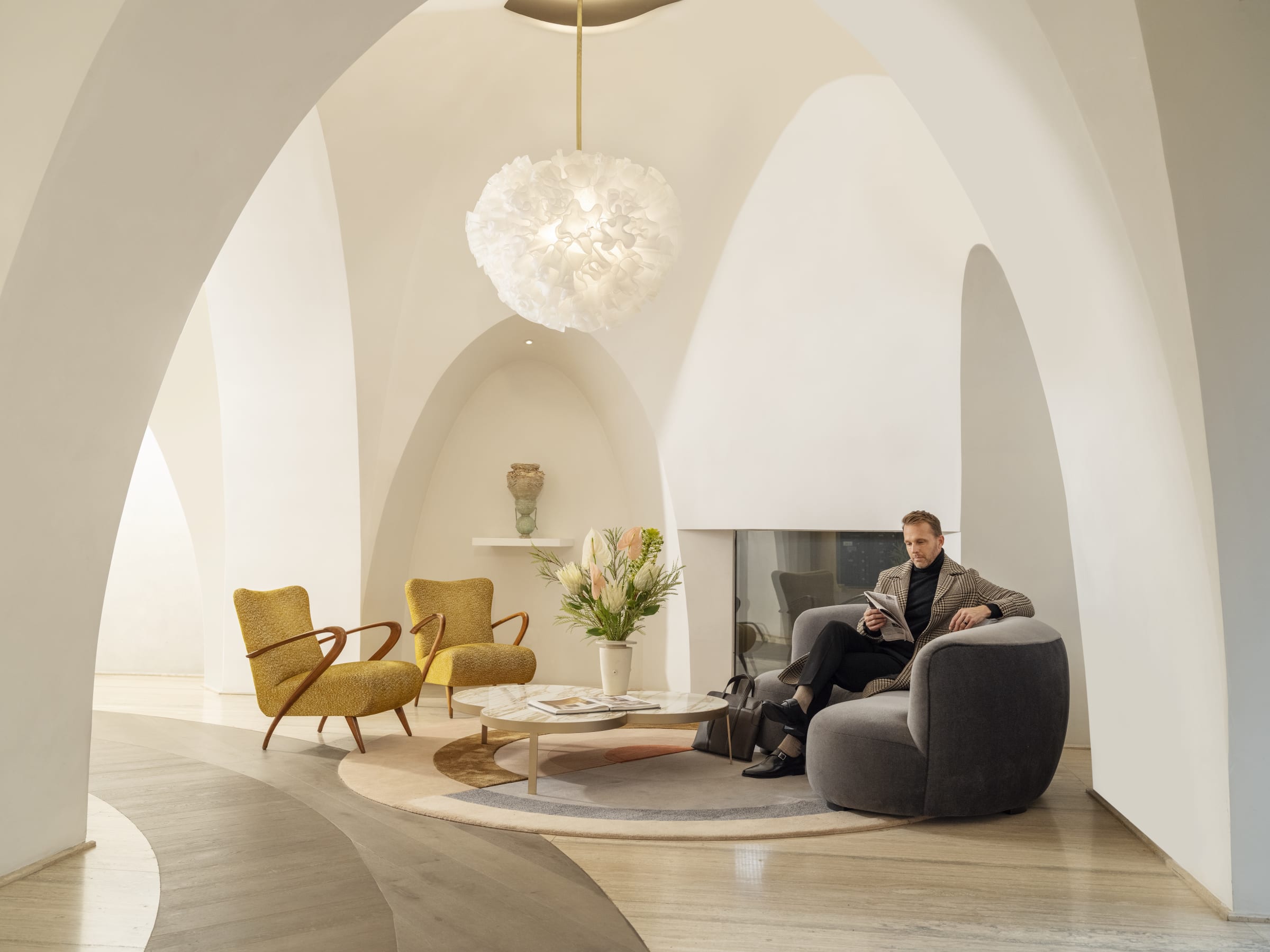 Gentleman sitting in the luxury lobby on a grey couch beneath dramatic archways of 180 E 88th Street, a luxury condominium on the upper east side of new york city in manhattan. 