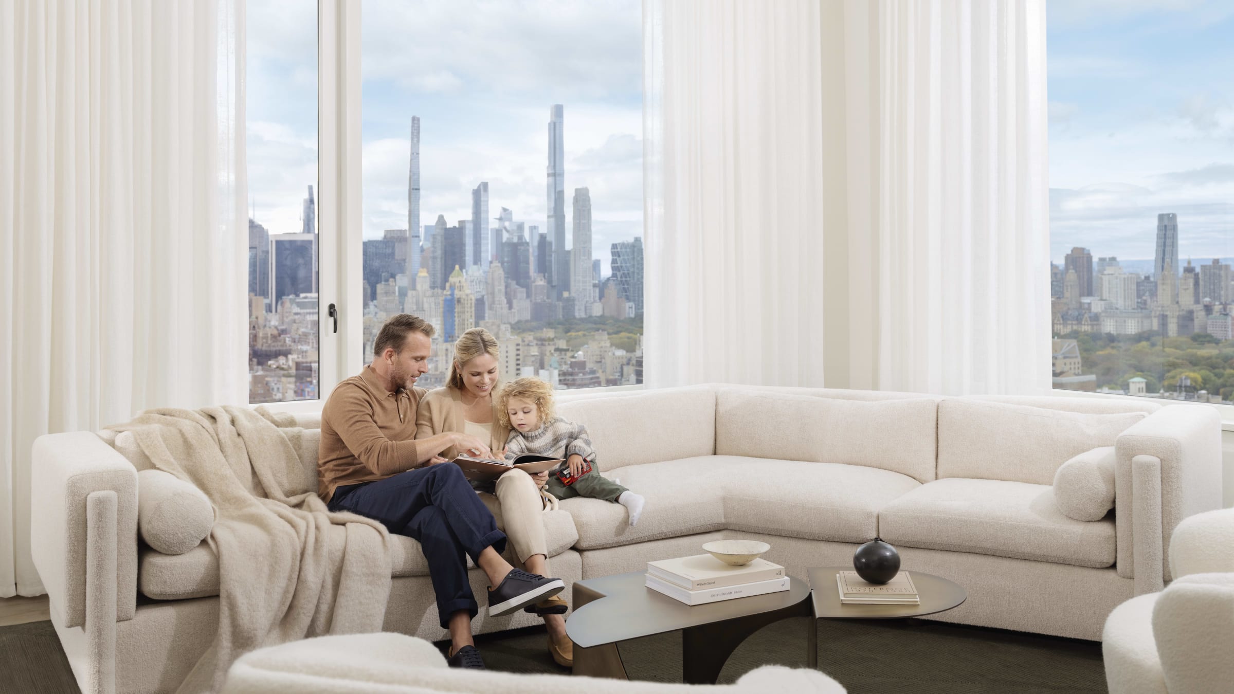 mother and father with child sitting on corner couch of living room in 180 e 88th street luxury east side condominium